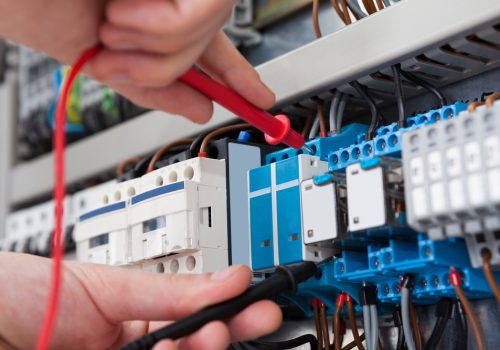 Closeup of male electrician examining fusebox with multimeter probe